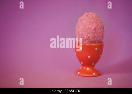 Rosafarbene Eiskugel in einer orangefarbenen Tasse mit Punktmuster vor einem weichen violetten Hintergrund für eine optisch ansprechende Dessertpräsentation Stockfoto