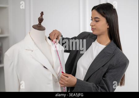 Langhaarige junge Frau mit einer weißen Jacke, die in einem Designstudio neben der Puppe steht Stockfoto
