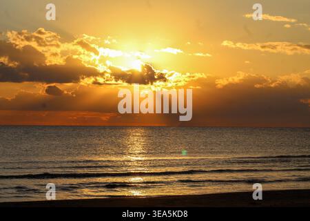 Golden Hour Sonnenaufgang beleuchtet Ozeanwellen mit warmem Licht und weichen Wolken in einer friedlichen Umgebung. Stockfoto