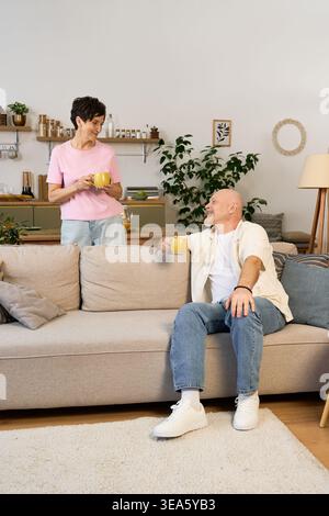 Ein liebevolles Seniorenpaar lacht fröhlich, während es in seinem einladenden Zuhause warme Getränke schlürft. Stockfoto