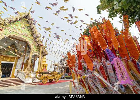 Dok kham Tai, Phayao, Thailand - 20. April 2026: Phra Chao Than Chai, vergoldetes Tor des Wat Si Chum mit orangefarbenen Tung-Bannern, thailändische Fahnen über dem Dach Stockfoto