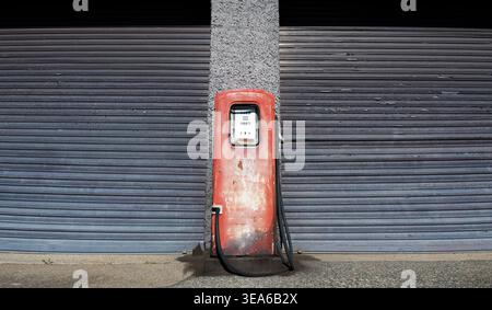 Eine alte, rote, rostige Gaspumpe vor einem einfachen Garagentor Stockfoto