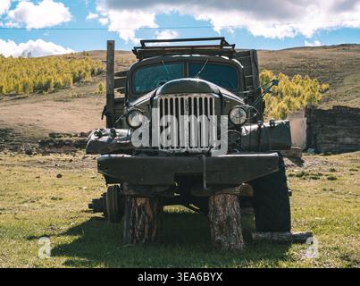 Ein alter Truck parkte auf grasbewachsenem Land unter blauem Himmel mit Wolken in der Nähe von Hügeln und Bäumen im Hintergrund Stockfoto