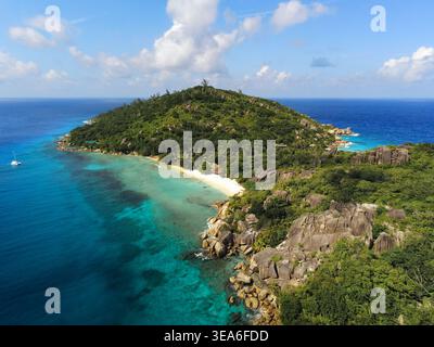 Blick aus der Vogelperspektive auf die Insel Grande Soeur mit üppigen grünen Hügeln, einem weißen Sandstrand und Granitfelsen entlang der türkisfarbenen Küste mit einem C Stockfoto
