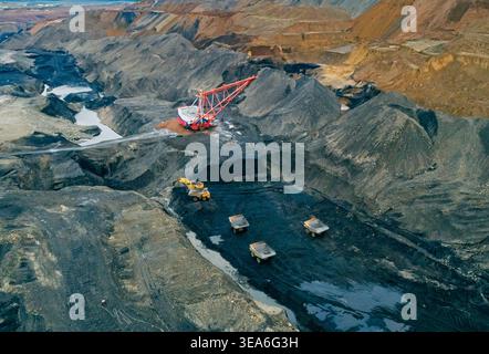 Panoramablick aus der Vogelperspektive erfasst den industriellen Kohlebergbau mit großem Schleppbagger und mehreren Transportfahrzeugen Stockfoto