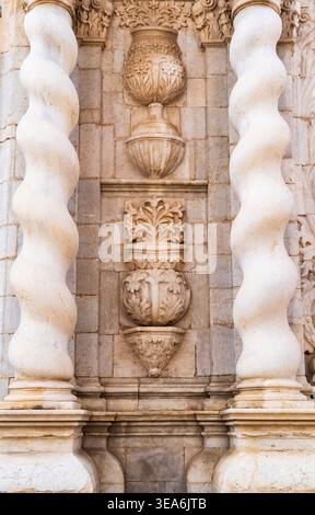 Verzierte Steinfassade mit verdrehten Spiralsäulen und geschnitzten Blumenreliefs auf historischer Architektur, symmetrische Nahaufnahme bei warmem Tageslicht. Stockfoto
