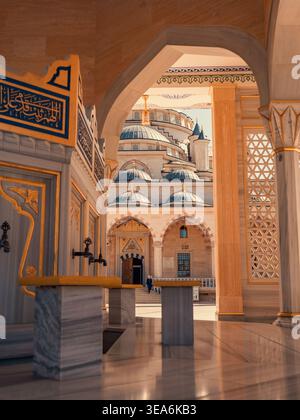 Grosny, Russland - 30. Juli 2021: Das Herz der Tschetschenischen Moschee durch einen bogenförmigen Eingang, der große Kuppeln und Marmorwaschanlagen enthüllt Stockfoto