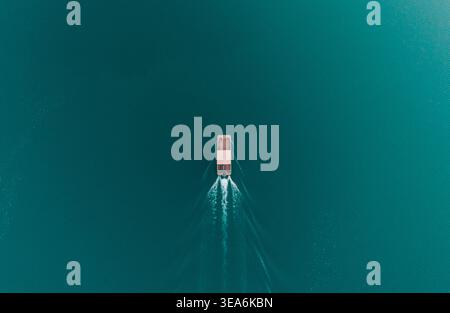 Aus der Vogelperspektive können Motorbootfahrten über ruhiges, blaublaues Wasser einfangen und an einem sonnigen Tag ein klares, weißes Licht hinterlassen Stockfoto