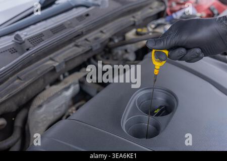 Überprüfung des Ölstands mit dem Ölmessstab im Fahrzeugmotor bei der routinemäßigen Fahrzeugwartung von Hand Stockfoto