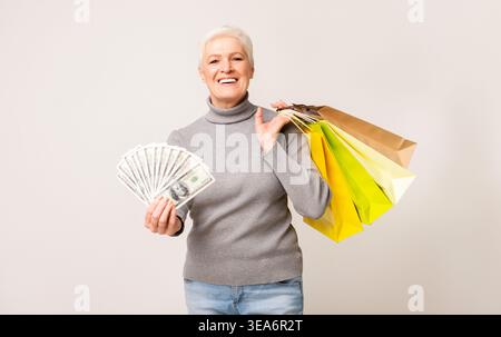 Glückliche Seniorin genießt Shopping mit Taschen und Bargeld in einer hellen Umgebung Stockfoto