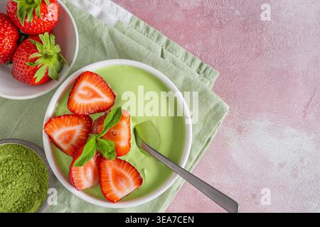 Matcha-Joghurt mit frischen Erdbeeren und Minzblättern in einer Schüssel mit einem Löffel. Draufsicht mit Kopierbereich. Gesundes Dessert, grünes Smoothie-Frühstück Stockfoto