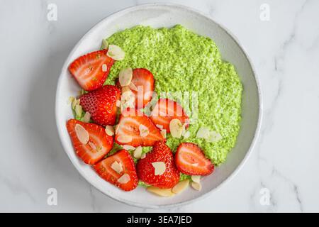 Blick von oben auf Matcha Chia Pudding mit frischen Erdbeeren und Mandelflocken in Keramikschale auf weißem Marmorhintergrund. Gesundes Dessert und vegetarisch Stockfoto