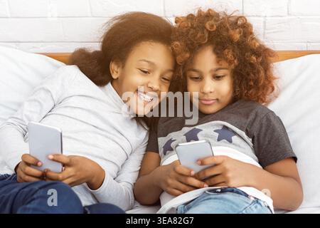 Beste Freunde, die am Telefon spielen, auf dem Bett liegen Stockfoto