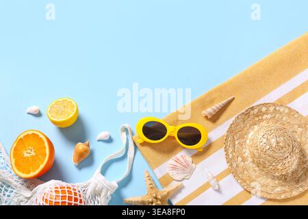 Strandtuch mit stilvoller Sonnenbrille, Schnur-Tasche mit frischen Zitrusfrüchten und Korbmütze auf blauem Hintergrund Stockfoto