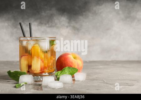 Glas leckerer Pfirsicheistee auf grauem Grunge-Hintergrund, Nahaufnahme Stockfoto