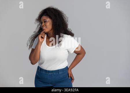 Afroamerikanerin im Studio posiert mit weißem geripptem Oberteil und blauer Jeans Stockfoto