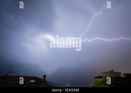 Blitze erleuchten ein dramatisches Gewitter über dem gardasee mit Bergen und Dächern darunter Stockfoto