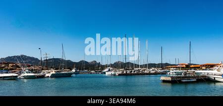 Yachten und Segelboote liegen im Hafen von Porto Rotondo in Sardinien, Italien, mit Küstenarchitektur und zerklüfteten Bergen unter einem klaren blauen Himmel. Stockfoto