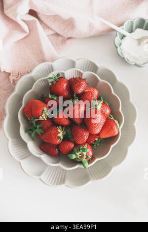 Helle und frische Komposition mit einer Schüssel reifer Erdbeeren, die auf einer gewellten Randplatte auf einem weißen Tisch platziert wird. Stockfoto