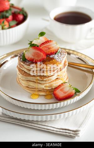 Einladende Frühstückskomposition mit einem Stapel goldener Pfannkuchen mit frischen Erdbeeren und Sirup, serviert auf einem weißen Teller Stockfoto