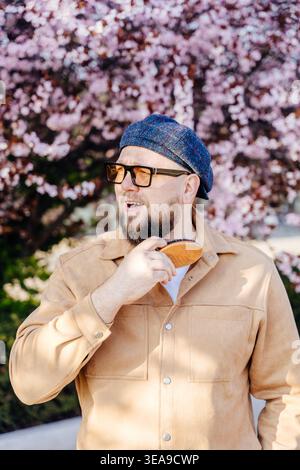 Lächelnder bärtiger Mann, der draußen unter blühenden Bäumen den Bart putzt Stockfoto