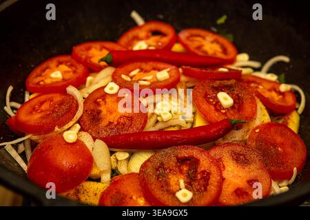 Kochen von Fleisch mit Tomaten, Chili, Knoblauch und Gemüse im gusseisernen Topf auf dem Herd Stockfoto