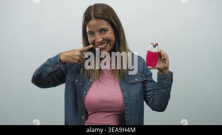Frau zeigt mit dem Finger auf die Zähne, während sie im Atelier eine rosa Zahnpasta-Flasche hält; vertrauensvolle Zahnpflege. Stockfoto