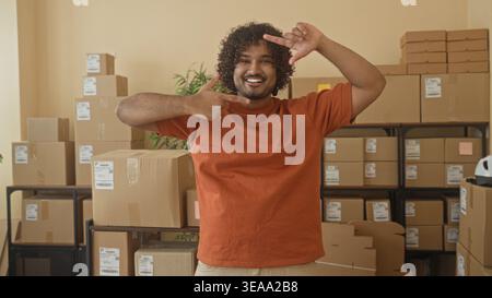 Mann, junger indischer Kleinunternehmer, der einen Karton mit offenen Armen hält und in einem Paketgebäude lächelt; Stolz auf Kleinunternehmen. Stockfoto