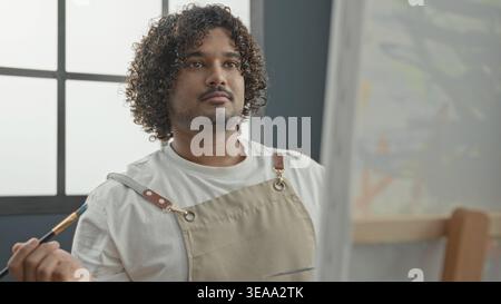 Junger indischer Maler malte mit Pinsel und Palette, während er Schürze im Atelier trug; ruhige Konzentration. Stockfoto
