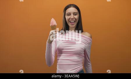 Frau, die Eisbecher hält und im Studio lächelt, mit rosafarbenem Servierteller, lässiger Oberseite und sichtbarer Waffeltasse, die von der Hand greift; verspielte Freude. Stockfoto