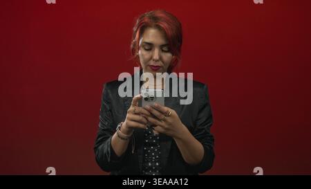 Frau tippt auf Smartphone in rotem Studio mit sichtbaren Fingern und schwarzem Blazer, Punktspitze; Konzentration. Stockfoto