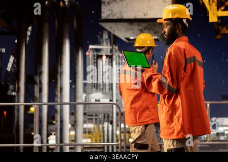 Isoliertes Modell mit einem Umweltbeauftragten inspiziert die Offshore-Ölplattform nachts und verwendet ein Tablet, um die Technik der Benzingewinnung zu überwachen. Strategie der Ölproduktion vom Ozean aus. Stockfoto