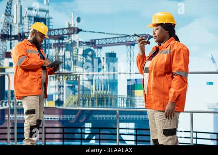 Ingenieurteam auf Offshore-Plattform mit tragbaren Funkgeräten zur Koordinierung der Schiffsoperationen. Frau auf Bohrgerät, die mit Kollegen spricht, indem sie Walkie Talkie verwendet, Teamwork-Konzept Stockfoto