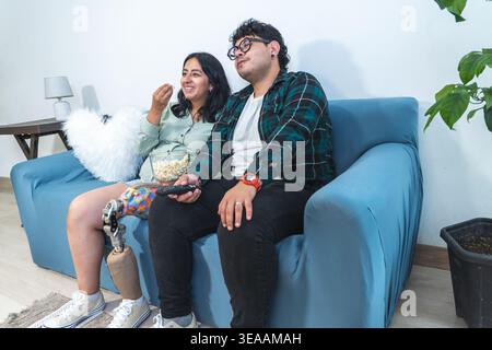 Glückliches Paar, das sich auf dem Sofa entspannt, Popcorn isst und gemeinsam Filme genießt Stockfoto