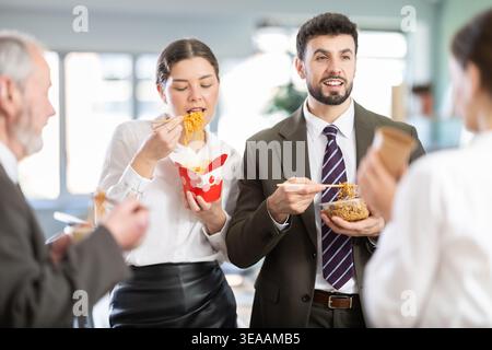Gruppe von freundlichen jungen Büroangestellten unterschiedlichen Alters, die in der modernen Bürokantine stehen und Fastfood essen Stockfoto