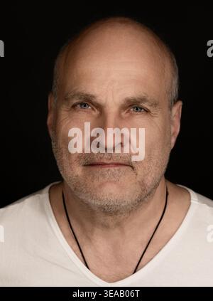 Reifer Mann mit Glatze und Stoppeln, der ein weißes Hemd auf schwarzem Hintergrund trägt Stockfoto