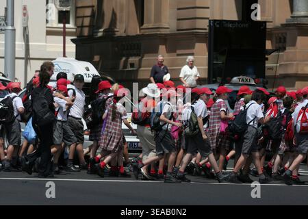 EINE GROSSE GRUPPE AUSTRALISCHER GRUNDSCHÜLER UND LEHRER ÜBERQUERT EINE VERKEHRSREICHE STRASSE IN SYDNEY, NEW SOUTH WALES, AUSTRALIEN. Stockfoto