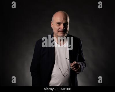 Ein reifer Mann steht, hält eine Brille und sieht in einem dunklen Studio in die Kamera Stockfoto