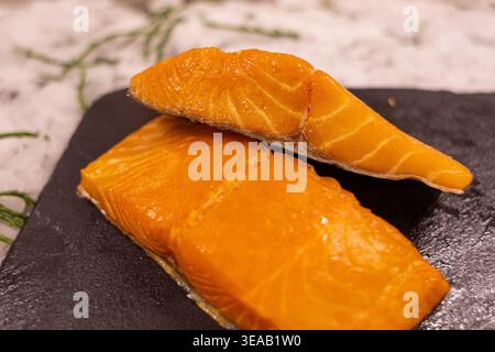 Zwei Stücke Lachs-Sushi werden auf eine schwarze Steinplatte gelegt. Das Sushi hat eine leuchtend orange Farbe und eine glatte Textur. Es ist zum Abendessen bereit. Stockfoto