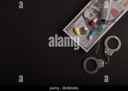 Spritze, Pillen, Handschellen und Dollarscheine auf dunklem Hintergrund. Konzept des Drogenhandels, illegaler Substanzen, Finanzkriminalität und Rechtsdurchsetzung Stockfoto