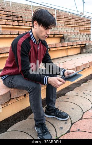 Junger Mann mit Tablette, der auf Stadionhaltern sitzt Stockfoto