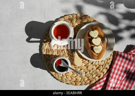 Frühstück in hartem Sonnenlicht mit Brot mit herzförmiger Butter, Marmelade und Tee, Kopierraum mit Blick von oben Stockfoto