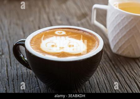 Blick von oben auf niedliche Katzengesicht Latte Art in schwarzer Keramikschale auf altem verwittertem Holzhintergrund. Minimalistisches rustikales Café, Kopie Sapce oben Stockfoto