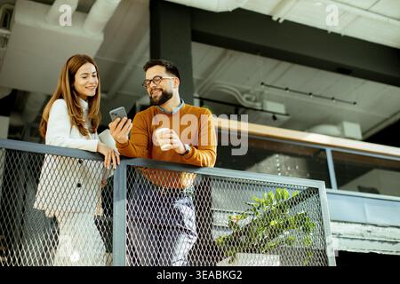 Zwei Kollegen teilen sich einen leichten Moment, diskutieren etwas auf einem Smartphone, während sie Kaffee in einem stilvollen Büro genießen. Stockfoto