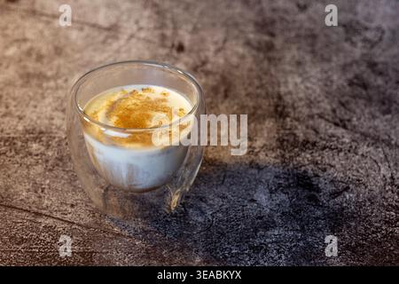 Seitenansicht von schmutzigem Kaffee in doppelwandigem Glas auf dunklem Betontisch. Industrie-Loft-Café-Stil mit dramatischer Seitenbeleuchtung. Stockfoto