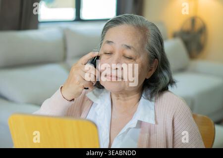 Schöne alte, reife asiatische Frau, die Spiegelreflexe genießt und Anti-Aging-Serum aufträgt. Eine Frau, die jeden Morgen die Schönheitsroutine macht. Selbstliebe-Konzept Stockfoto