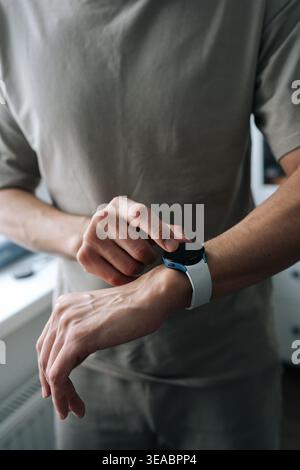 Nahaufnahme eines Mannes mit Smartwatch. Der Finger berührt den Bildschirm am Handgelenk. Modernes tragbares Gerät für Fitness und Kommunikation. Neutrale Farben, weiches natürliches Stockfoto