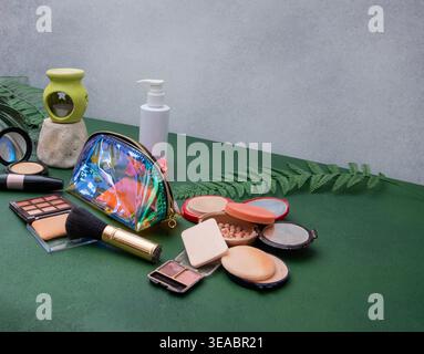 Arrangement für Kosmetikprodukte und Make-up-Tools. Streukollektion mit schillerndem Beutel, Lidschatten-Palette und Kosmetik auf grünem grauen Hintergrund. Stockfoto