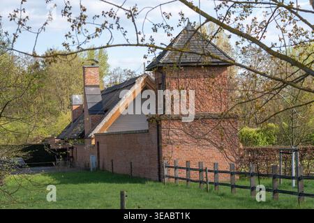 Der rote Backsteinturm steht hoch neben der rustikalen Dachlinie. Grünes Gras wächst in der Nähe von Holzzaun und Steinpfaden. Baumzweige Rahmen die Ansicht oberhalb der alten Stockfoto