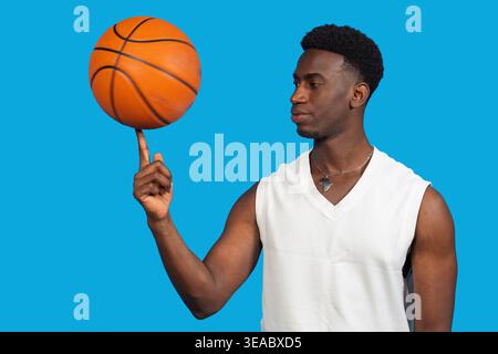 Junger Mann, der geschickt einen Basketball auf seinem Finger vor blauem Hintergrund dreht Stockfoto